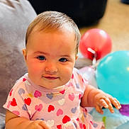 Noa joined the competition — help win amazing prizes! baby, child, infant, heart_pattern, dress, balloons, indoor, couch, smiling, happy, cute, chubby_cheeks, person, portrait, seated, colorful, playtime, soft_light, young, fun