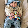 baby, child, hat, blue_hat, toy, smile, cushioned_chair, clothing, cozy, indoor, cute, face, person, pants, sitting, playful, embroidered, patterned_clothing, happy, hands