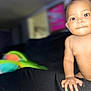 baby, black_surface, blurred_background, child, closeup, colorful_toys, cute, expression, eyes, face, fingers, hand, indoor, infant, nose, person, portrait, sitting, skin, young