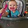 baby, high_chair, face_paint, food, spoon, messy, smiling, blue_shirt, floral_pattern, happy, child, indoor, feeding, cute, infant, table, person, expression, playful, mealtime