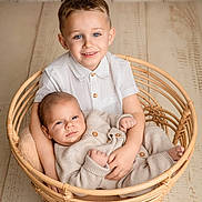 Zack participe au concours pour gagner de l'argent avec cette photo : baby, child, siblings, basket, wicker, portrait, smile, blue_eyes, neutral_colors, wooden_floor, indoor, family, cute, holding, clothing, buttoned_shirt, knitwear, happy, infant, toddler