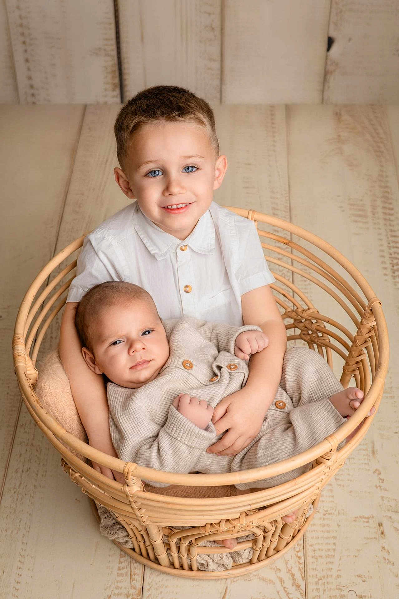 Zack participe au concours pour gagner de l'argent avec cette photo : baby, child, siblings, basket, wicker, portrait, smile, blue_eyes, neutral_colors, wooden_floor, indoor, family, cute, holding, clothing, buttoned_shirt, knitwear, happy, infant, toddler