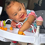 Laveah is registered to the contest to win money with this photo: baby, toddler, child, walker, toy, snack, cheese_puffs, smiling, happy, indoor, clothing, hair_bun, face, hand, seat, playful, colorful, person, infant, cute