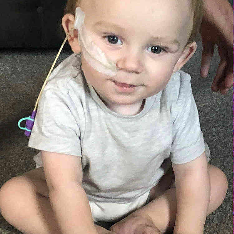 Bayley joined the competition — help win amazing prizes! baby, carpet, casual_clothing, child, cross_legged, cute, face, floor, hands, healthcare, home, indoor, infant, medical_device, nasal_tube, person, short_hair, sitting, supporting_hands, young_child