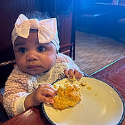 Niori joined the competition — help win amazing prizes! appetite, baby, biscuit, bow, child, clothing, cozy, curious, face, food, hands, headband, indoor, light, person, plate, restaurant, sitting, table, wood