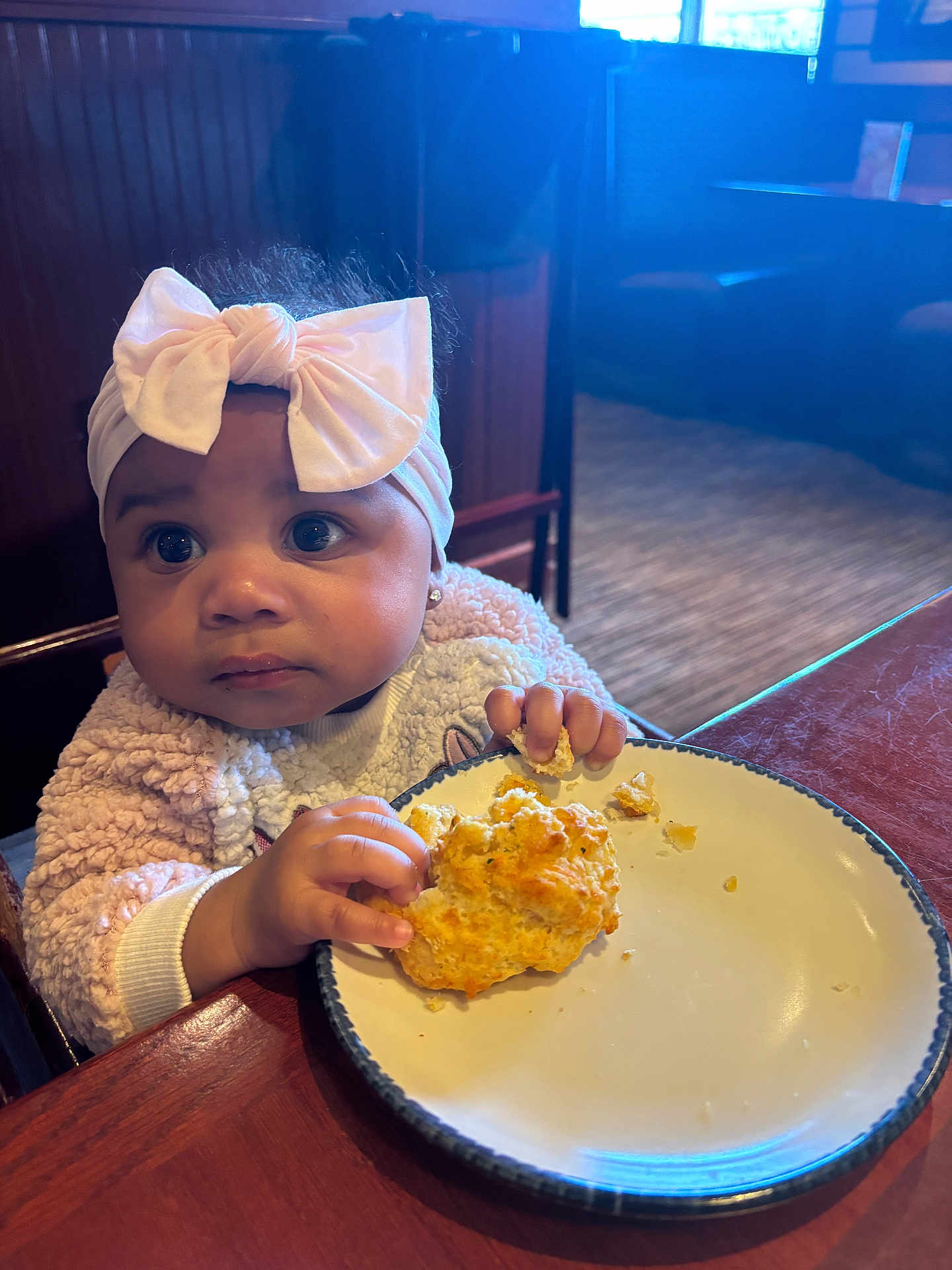 Niori joined the competition — help win amazing prizes! appetite, baby, biscuit, bow, child, clothing, cozy, curious, face, food, hands, headband, indoor, light, person, plate, restaurant, sitting, table, wood