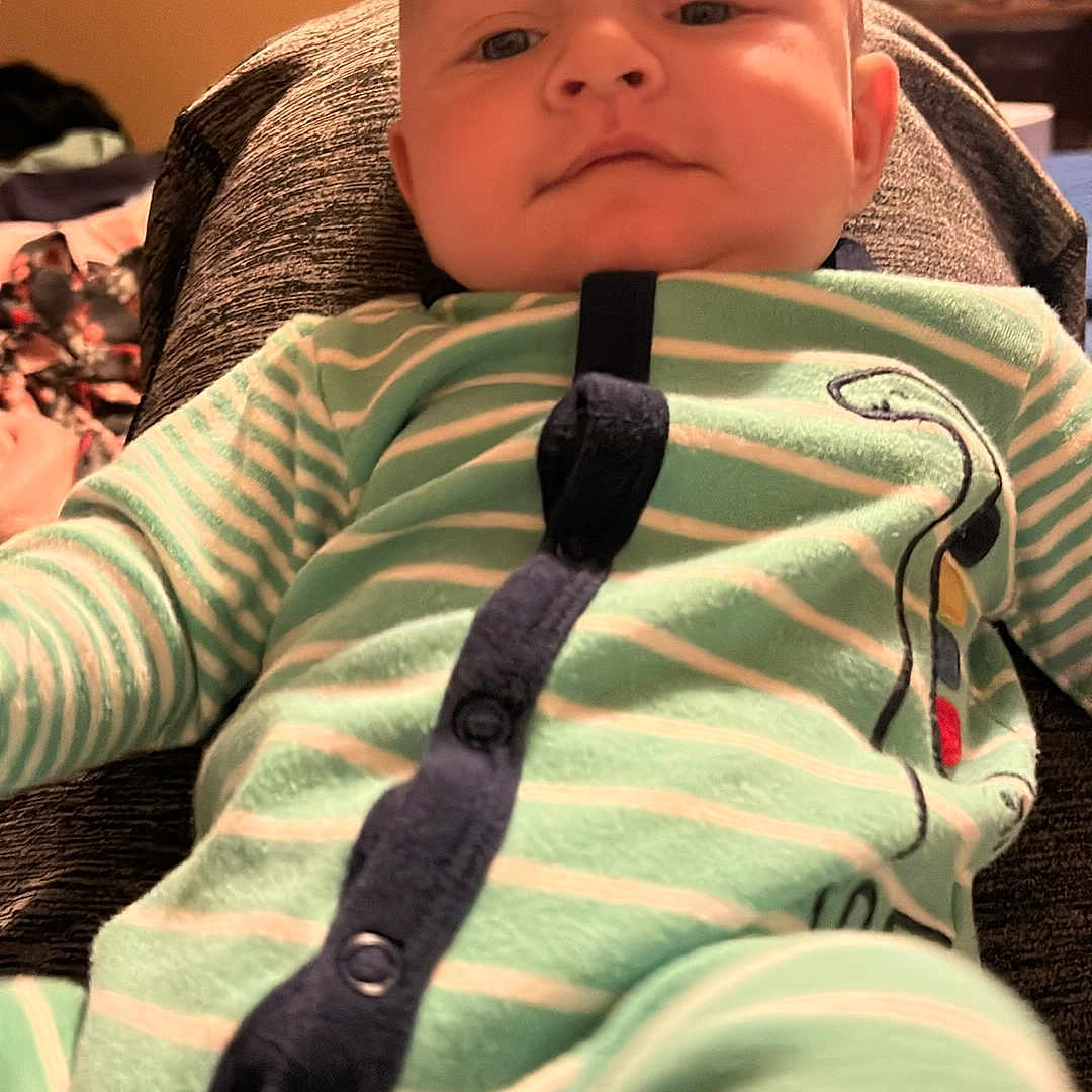 Layne joined the competition — help win amazing prizes! baby, infant, child, portrait, sitting, car_seat, pajamas, striped_clothing, green_clothing, indoor, home, living_room, television, furniture, head, face, serious_expression, looking_at_camera, close_up, photography
