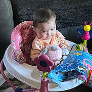Evelyn is registered to the contest to win money with this photo: baby, child, infant, sitting, activity_center, jumper, baby_toy, colorful, butterfly, flower_toy, plush_toy, playroom, indoors, couch, blanket, wood_floor, portrait, curious, baby_clothing, smiling