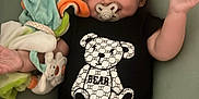 Ilyess a rejoint le concours — aidez-le/la à gagner de superbes lots ! baby, bear_design, black_clothing, child, colorful, comfort, cushion, cute, happy, indoor, infant, lying_down, onesie, pacifier, plush_toy, portrait, smiling, soft_toys, toddler, toy