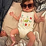 apparel, baby, bed, blanket, casual, child, comfort, cute, fashion, headwear, indoor, infant, lying_down, onesie, pattern, person, sleepwear, small_child, sunglasses, vegetables