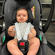Arya is registered to the contest to win money with this photo: baby, car_seat, infant, child, straps, onesie, bracelet, black, playful, tongue_out, indoor, seat_belt, safety, cute, legs, hands, head_support, fabric, person, closeup
