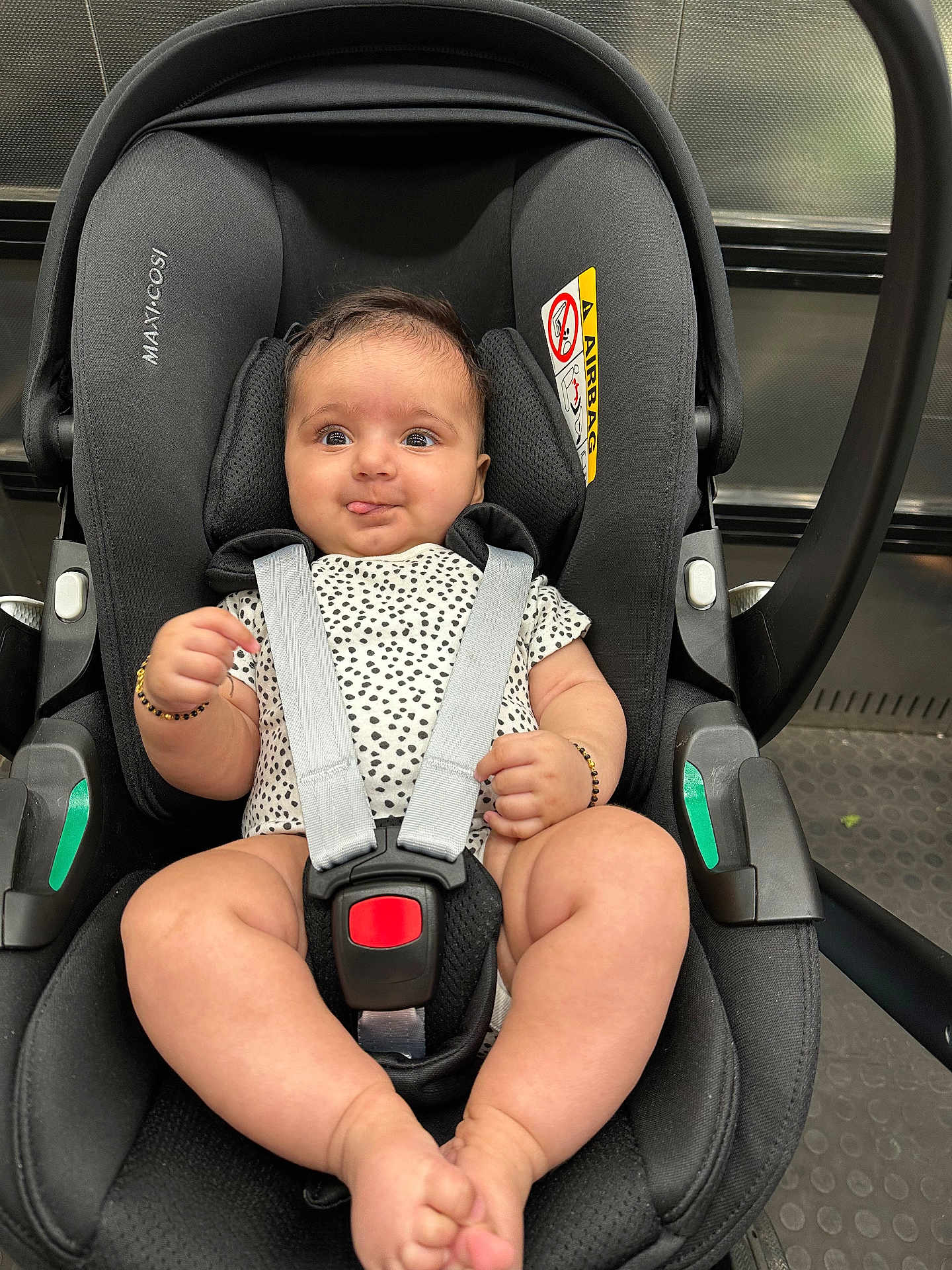 Arya is registered to the contest to win money with this photo: baby, car_seat, infant, child, straps, onesie, bracelet, black, playful, tongue_out, indoor, seat_belt, safety, cute, legs, hands, head_support, fabric, person, closeup