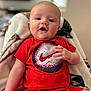 baby, infant, child, red_clothing, baseball_graphic, blanket, sitting, indoors, portrait, cute, face, hand, short_sleeves, shorts, person, young_child, cozy, expression, looking_at_camera, comfortable