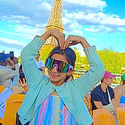 Jasleen a rejoint le concours — aidez-le/la à gagner de superbes lots ! child, girl, sunglasses, heart_pose, eiffel_tower, landmark, outdoor, blue_sky, clouds, people, tourists, stadium_seats, colorful_clothing, pastel_colors, knit_sweater, smiling, daytime, trees, photography, happy