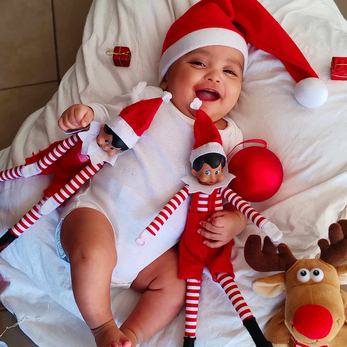 Evan David a rejoint le concours — aidez-le/la à gagner de superbes lots ! baby, child, christmas, clothing, cute, elf_doll, festive, floor, happy, holiday, indoor, infant, playful, portrait, red, reindeer_plush, santa_hat, smiling, toy, white_blanket