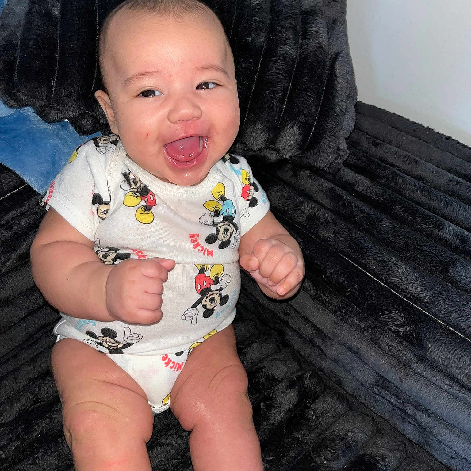 Xavier joined the competition — help win amazing prizes! baby, infant, smiling, happy, mickey_mouse, onesie, clothing, couch, furniture, indoor, skin, face, cute, child, person, seated, plush, texture, joy, expression