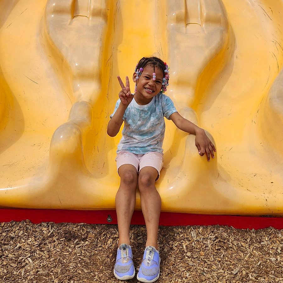 Zariah is registered to the contest to win money with this photo: child, clothing, face, female, footwear, girl, grass, head, nature, outdoorplayarea, outdoors, park, person, photography, playarea, portrait, shoe, shorts, slide, toy