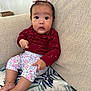 Ailani is registered to the contest to win money with this photo: baby, child, infant, couch, sofa, blanket, flower_headband, maroon_clothing, floral_pants, sitting, indoors, curious_expression, wide_eyes, small_hands, barefoot, home_interior, cozy, furniture, person, portrait