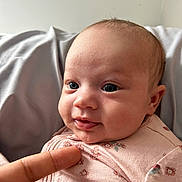 Jerzy is registered to the contest to win money with this photo: baby, infant, face, eyes, smile, pink_clothing, floral_pattern, hand, finger, skin, portrait, cute, child, newborn, person, closeup, soft_light, indoors, expression, young