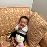 Ivanna joined the competition — help win amazing prizes! baby, child, smiling, happy, sitting, toy, stuffed_animal, plush, couch, patterned_fabric, clothing, indoors, home, infant, hands, face, foot, wall, pillow, rattle