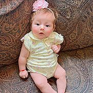 Aylani is registered to the contest to win money with this photo: baby, child, infant, portrait, sitting, couch, upholstery, floral_outfit, headband, flower, hair, face, eyes, smile, surprised, indoors, home, patterned_background, bracelet, photography
