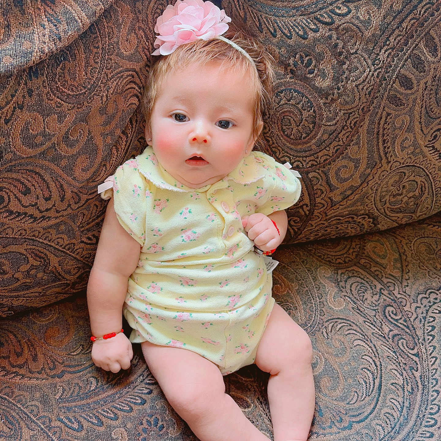 Aylani is registered to the contest to win money with this photo: baby, child, infant, portrait, sitting, couch, upholstery, floral_outfit, headband, flower, hair, face, eyes, smile, surprised, indoors, home, patterned_background, bracelet, photography