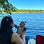 baby, woman, lake, water, blue_sky, smiling, hooded_outfit, striped_clothing, nature, trees, leaves, outdoor, joy, laughing, person, child, seated, blanket, chair, sunlight