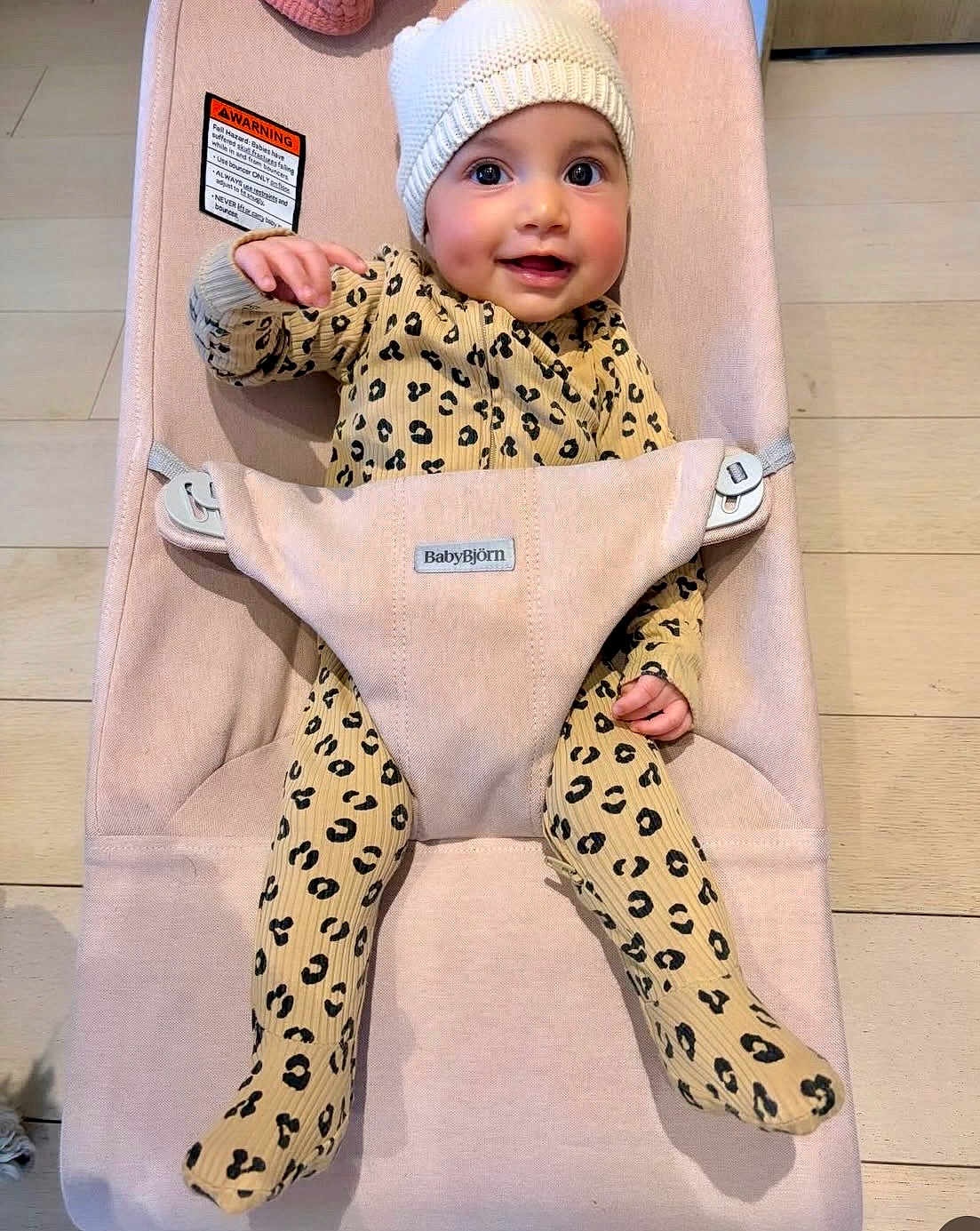 Kaia joined the competition — help win amazing prizes! baby, infant, child, smiling, beanie, hat, bouncer, babybjorn, leopard_print, onesie, harness, wooden_floor, rosy_cheeks, big_eyes, hand, feet, indoor, seat, cozy, portrait
