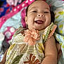 baby, smiling, infant, dress, flower, blanket, happy, child, cute, portrait, face, skin, hand, lying_down, colorful, pattern, fabric, person, indoors, closeup