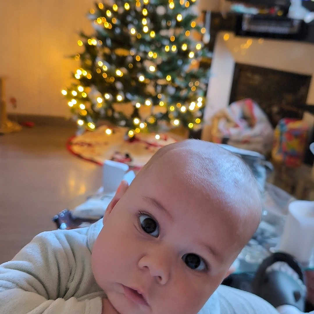 Kynaï participe au concours pour gagner de l'argent avec cette photo : baby, background_blur, child, christmas_tree, clothing, cozy, curious, cute, expression, face, festive, holiday, home, indoors, infant, lights, person, portrait, soft_focus, warm_lighting