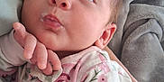 Lily is registered to the contest to win money with this photo: baby, infant, face, hand, onesie, floral_pattern, blanket, person, skin, cute, newborn, sleepwear, expression, comfort, soft, closeup, portrait, indoors, resting, cozy