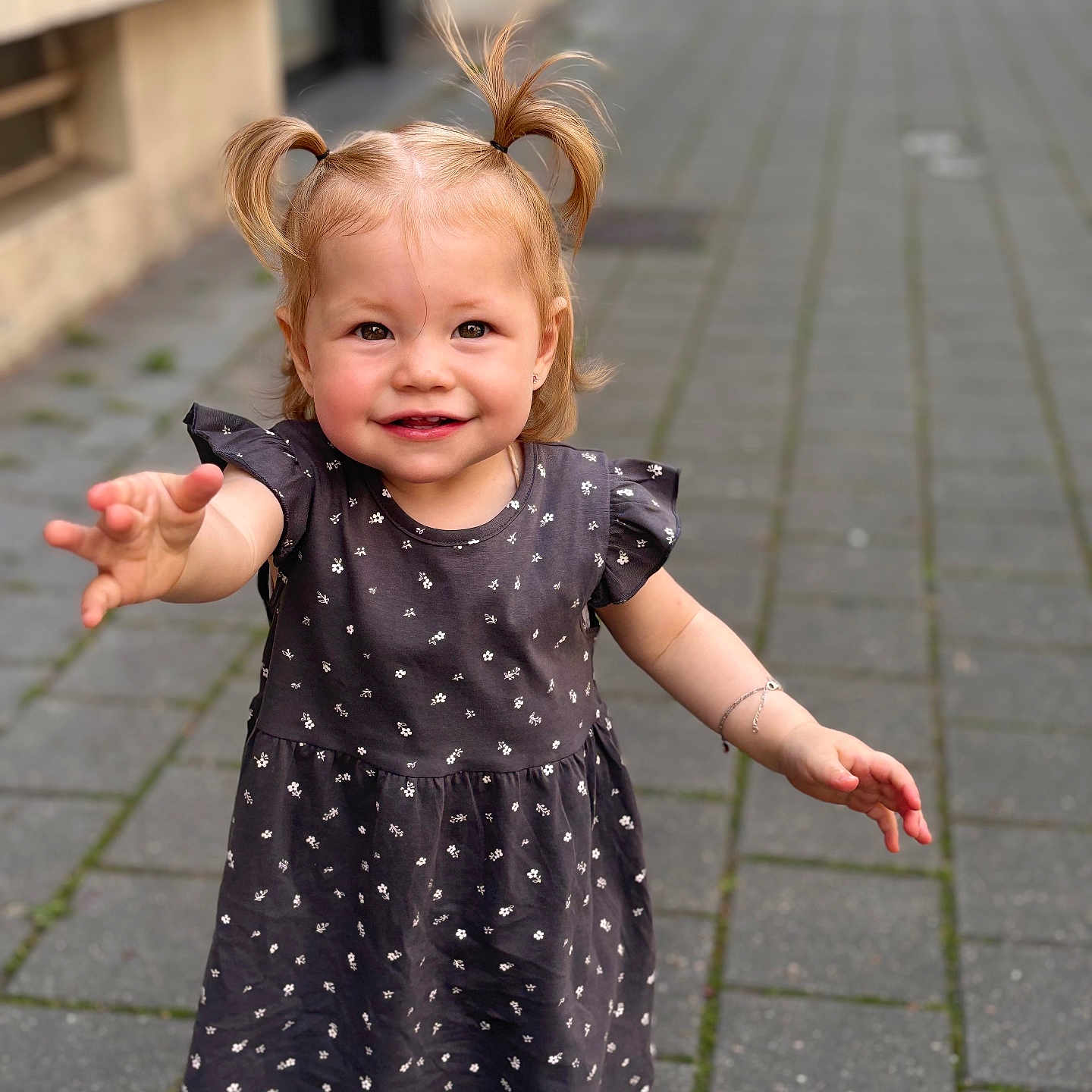 Luciana participe au concours pour gagner de l'argent avec cette photo : blonde_hair, bracelet, casual_clothing, child, cute, daylight, dress, happy, outdoor, pavement, person, pigtails, portrait, reaching_hand, sidewalk, small_flower_pattern, smiling, toddler, walking, young_child