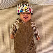 Lewis a rejoint le concours — aidez-le/la à gagner de superbes lots ! baby, smiling, crown, corduroy, overalls, striped_shirt, lying_down, happy, child, infant, face, headwear, cute, indoors, fabric, person, one_person, portrait, playful, cozy