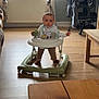 Naël a rejoint le concours — aidez-le/la à gagner de superbes lots ! baby, walker, living_room, curtains, window, wooden_floor, table, chair, computer, monitor, desk, bib, toy, footwear, person, indoor, home, furniture, flooring, light