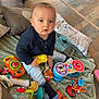 toddler, child, toys, playtime, blanket, floor, cushions, indoor, baby, colorful, camera_toy, clothing, socks, wooden_floor, expression, sitting, curious, person, home, cute