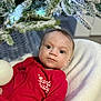 Oscar is registered to the contest to win money with this photo: baby, infant, red_clothing, christmas_tree, ornament, holiday, festive, blanket, face, eyes, expression, indoors, winter, decorations, cute, portrait, child, seasonal, celebration, cozy