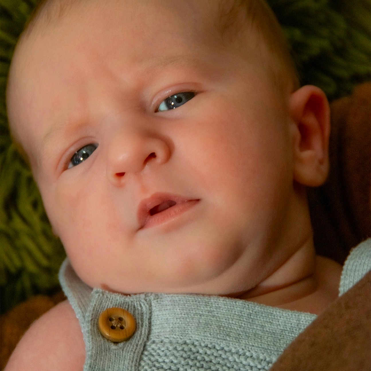 Bennett is registered to the contest to win money with this photo: baby, blanket, blue_eyes, button, child, close_up, ear, expression, face, head, indoors, infant, knitted_clothing, newborn, person, portrait, puzzled, skin, soft, texture