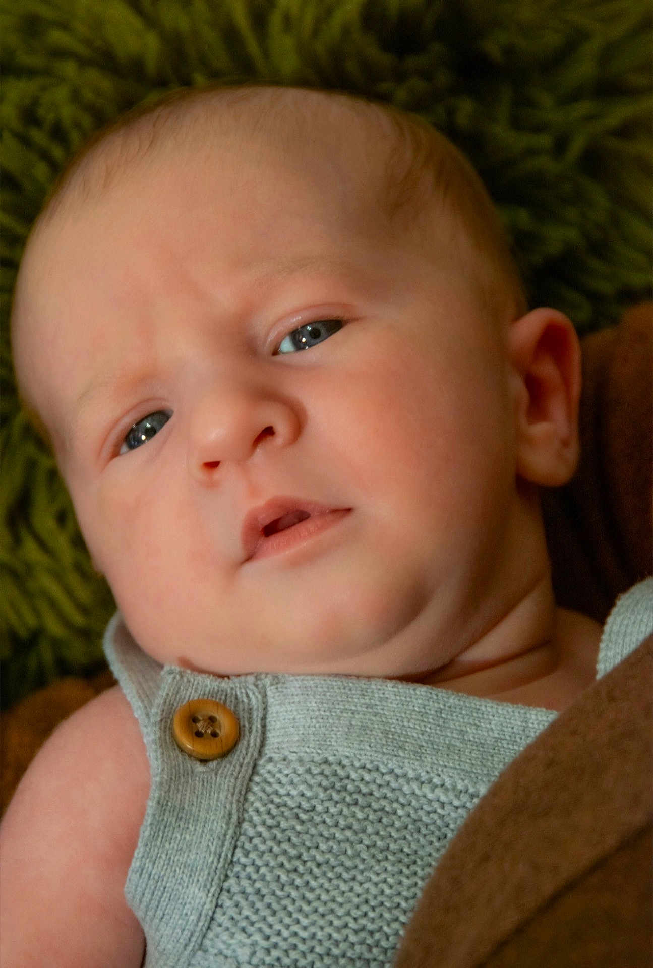 Bennett is registered to the contest to win money with this photo: baby, close_up, face, infant, knitted_clothing, button, blue_eyes, expression, puzzled, skin, head, ear, blanket, texture, soft, portrait, child, newborn, indoors, person
