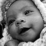 baby, close_up, black_and_white, smiling, face, infant, blanket, hood, cute, portrait, soft_texture, warm, newborn, cozy, expression, eyes, cheeks, child, wrapped, peaceful