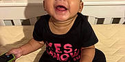 Xaviera joined the competition — help win amazing prizes! baby, laughing, crib, mattress, black_clothing, white_socks, remote_control, happy, child, indoor, portrait, smiling, headband, decor, photograph, wall, furniture, person, infant, cute