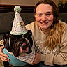 woman, dog, bulldog, party_hat, bandana, smiling, indoor, couch, celebration, casual_clothing, long_hair, portrait, pet, companion, happy, cozy, home, ripped_jeans, hand, friendship