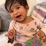 Sanvi joined the competition — help win amazing prizes! baby, toddler, smiling, happy, child, indoors, toy, colorful, ball, face, hair, clothing, pajamas, pattern, bed, cushion, person, cute, playful, young