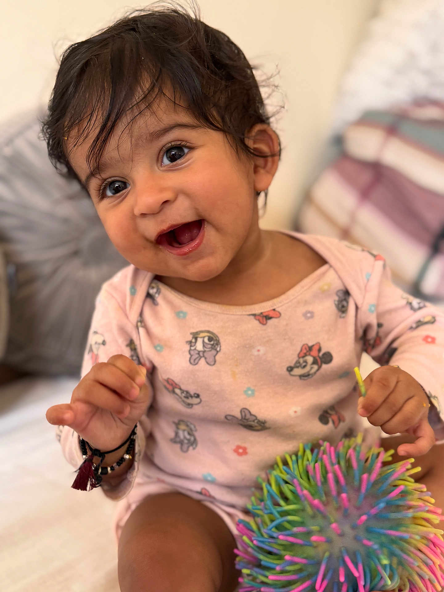 Sanvi joined the competition — help win amazing prizes! baby, toddler, smiling, happy, child, indoors, toy, colorful, ball, face, hair, clothing, pajamas, pattern, bed, cushion, person, cute, playful, young