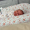 baby, smiling, swaddled, blanket, floral_pattern, cushion, playpen, infant, sleeping, cozy, bedroom, face, head, comfort, cute, child, newborn, resting, indoors, soft