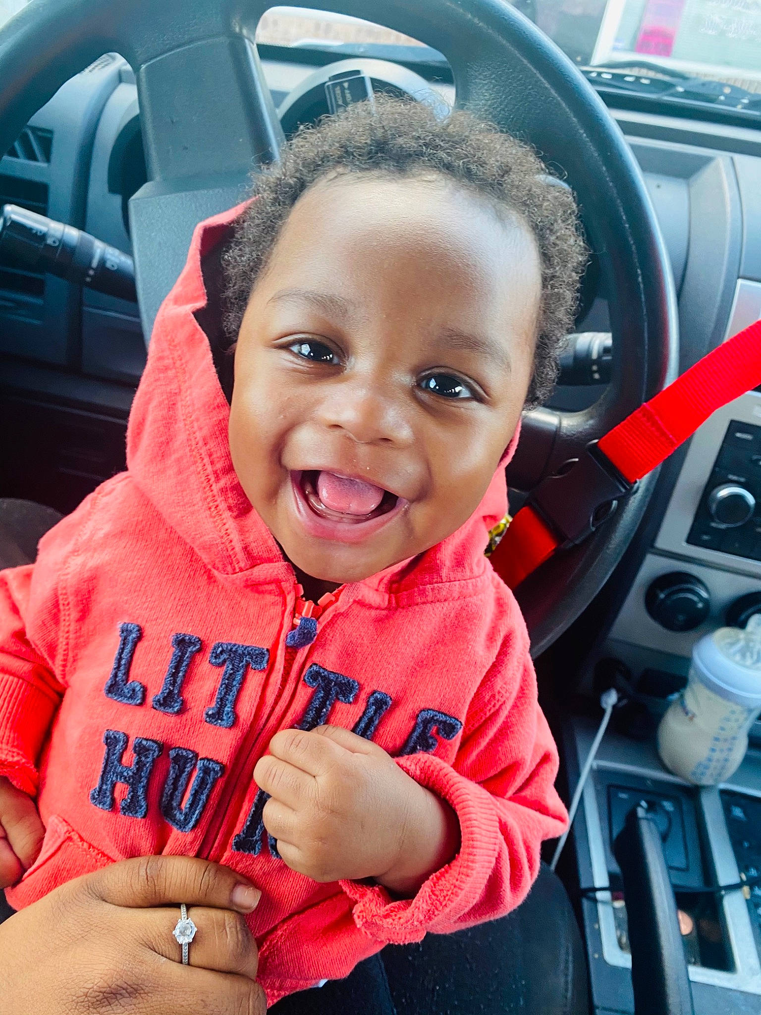 Kamron is registered to the contest to win money with this photo: automotive_design, automotive_exterior, car_seat, car_seat_cover, chin, eye, face, gesture, happy, joy, motor_vehicle, person, personal_luxury_car, skin, sleeve, smile, steering_wheel, thumb, toddler, vehicle