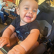 Tre is registered to the contest to win money with this photo: baby, smile, hands, stroller, indoor, restaurant, people, man, table, chair, drink, clothing, face, person, happy, child, casual, background, light, curly_hair