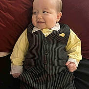 Leo joined the competition — help win amazing prizes! baby, child, smile, face, clothing, suit, vest, shirt, pinstripe, yellow_shirt, cushion, red_background, lying_down, hand, portrait, cute, infant, happy, indoors, person