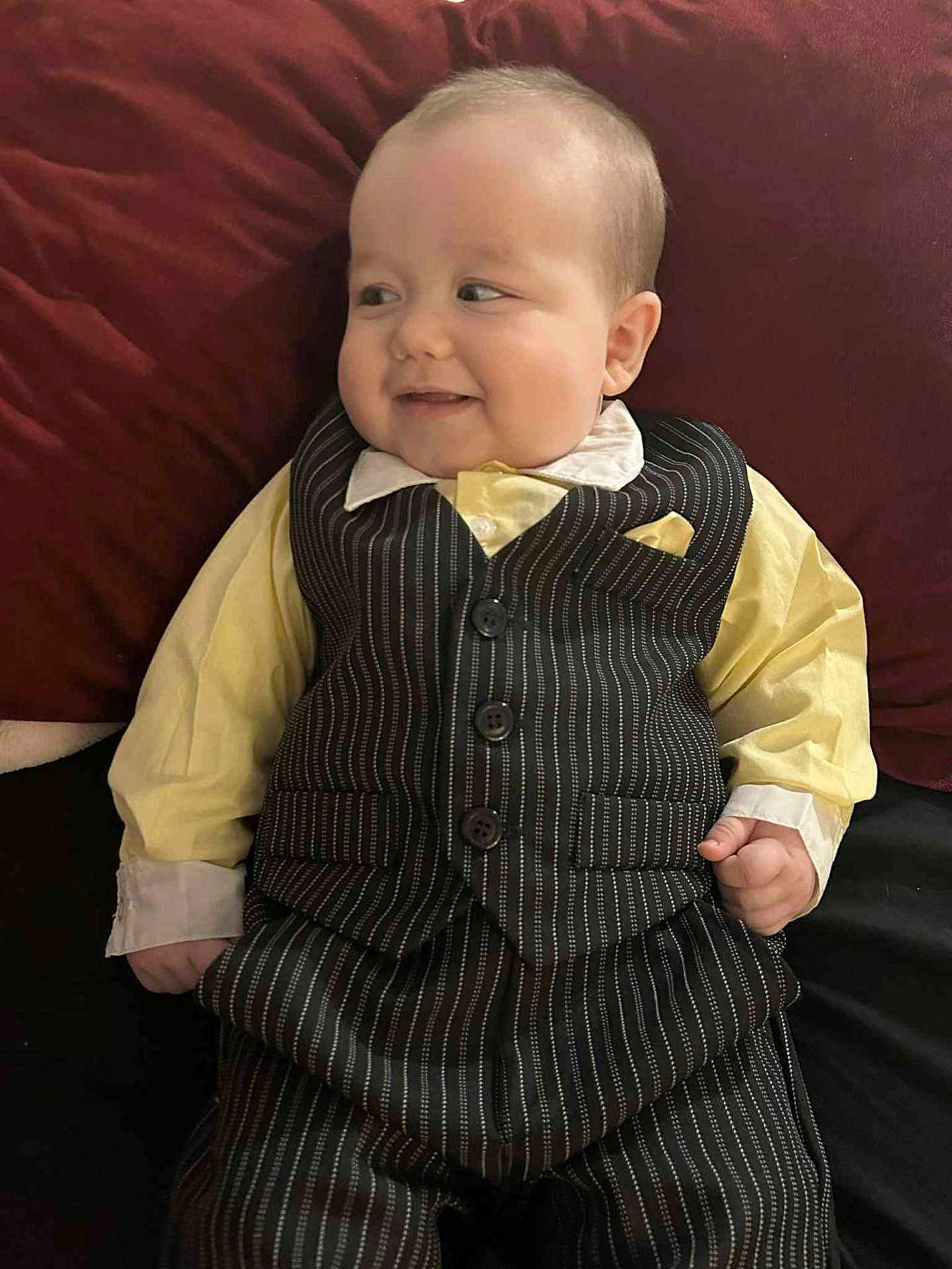 Leo joined the competition — help win amazing prizes! baby, child, smile, face, clothing, suit, vest, shirt, pinstripe, yellow_shirt, cushion, red_background, lying_down, hand, portrait, cute, infant, happy, indoors, person