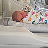 newborn, baby, hospital, bassinet, blanket, duck_pattern, wrapped, infant, bed, healthcare, curtains, face, person, sleeping, swaddled, white, plastic, resting, cute, tiny
