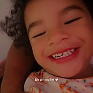 Seilose Brianna is registered to the contest to win money with this photo: child, smiling, closeup, curly_hair, happy, person, face, patterned_clothing, arm, indoor, portrait, cute, joyful, young_child, casual, cozy, intimate, expression, text_overlay, colorful
